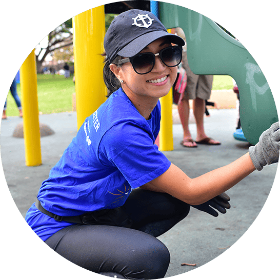 Young adult woman in blue Blue Zones Project shirt cleaning a playground