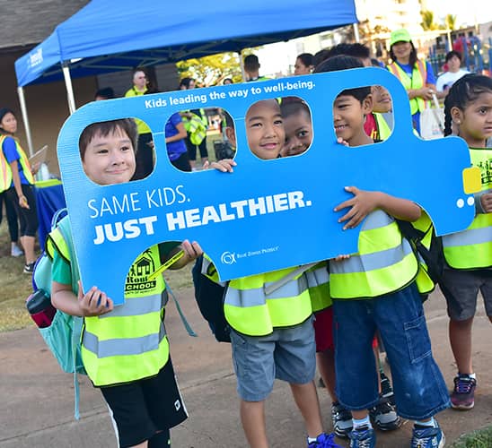 Young children in yellow safety vests holding a cardboard cutout of a school bus