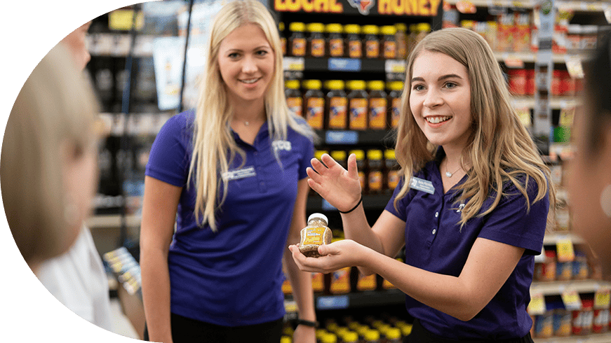Two employees at a grocery store showing a product to customers